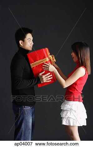 Young man holding gift, facing young woman View Large Photo Image Stock Photo - Young man holding gift, facing young woman. Fotosearch