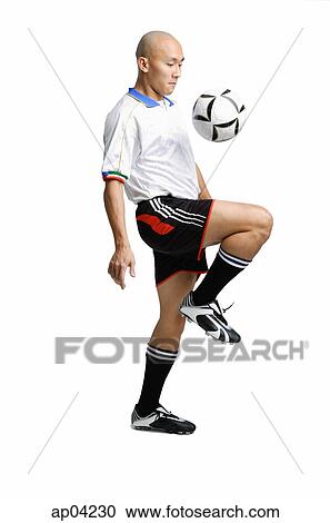 Stock Image - Young man in soccer uniform, using knee to hit ball. Fotosearch