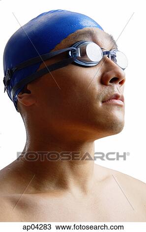 Stock Image - Young man wearing swimming cap and goggles, head shot . Fotosearch