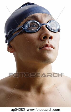 Stock Image - Young man with swimming cap and goggles, head shot. Fotosearch
