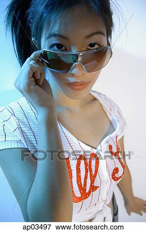 Stock Photo - Young woman adjusting sunglasses, looking at camera . Fotosearch