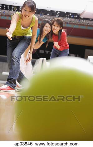 Stock Photograph - Young woman bowling, friends watching behind her . Fotosearch