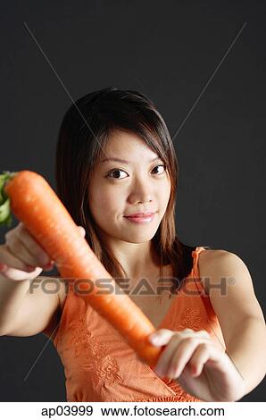 Young woman holding carrot, looking at camera View Large Photo Image Stock Photo - Young woman holding carrot, looking at camera . Fotosearch