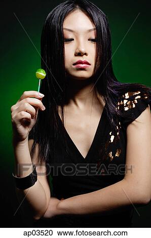 Young woman in black dress, holding green lollipop, arms crossed View Large Photo Image Stock Image - Young woman in black dress, holding green lollipop, arms crossed . Fotosearch