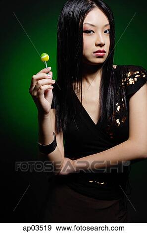 Stock Photo - Young woman in black dress, holding green lollipop . Fotosearch