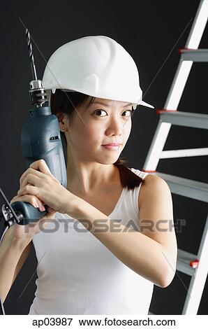 Stock Photo - Young woman in hard hat, holding drill . Fotosearch