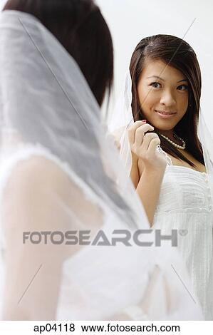Young woman in white dress and veil, looking at mirror View Large Photo Image Stock Photo - Young woman in white dress and veil, looking at mirror. Fotosearch