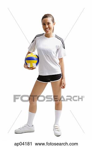 Stock Image - Young woman standing and holding volleyball. Fotosearch