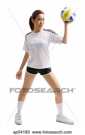 Stock Image - Young woman standing, holding volleyball in one hand. Fotosearch
