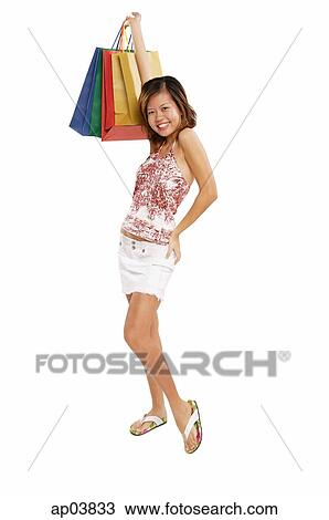 Stock Image - Young woman standing with hand on hip, carrying shopping bags . Fotosearch