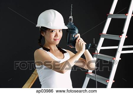 Stock Photograph - Young woman wearing hard hat, holding drill . Fotosearch