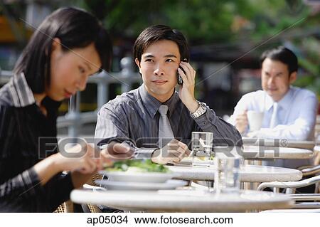 Business people at outdoor café, focus on man with mobile phone View Large Photo Image Stock Photo - Business people at outdoor café, focus on man with mobile phone. Fotosearch - Search Stock Images, Mural Photographs, Pictures, and Clipart Photos