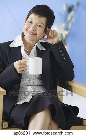 Business woman sitting on chair, holding mug View Large Photo Image Stock Image - Business woman sitting on chair, holding mug. Fotosearch