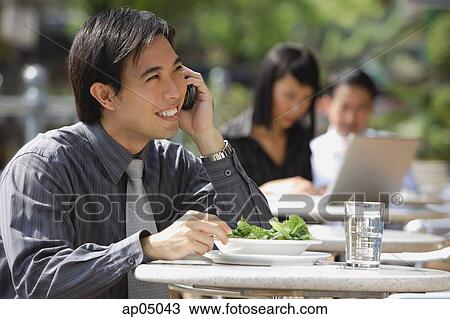 Stock Image - Businessman having lunch at outdoor cafe, using mobile phone. Fotosearch