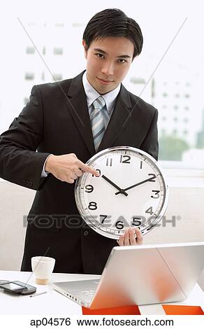 Stock Photograph - Businessman holding and pointing at clock. Fotosearch