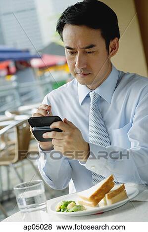 Stock Photo - Businessman in cafe, using PDA. Fotosearch
