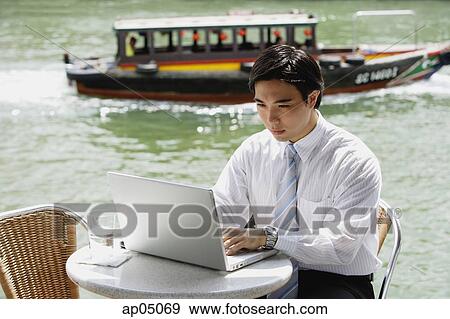 Businessman sitting at outdoor cafe, using laptop, river in the background View Large Photo Image Stock Photo - Businessman sitting at outdoor cafe, using laptop, river in the background. Fotosearch
