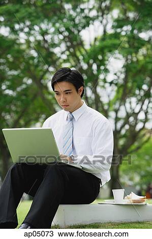 Businessman sitting in park, using laptop View Large Photo Image Stock Image - Businessman sitting in park, using laptop. Fotosearch