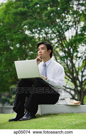 Picture - Businessman sitting in park with laptop. Fotosearch