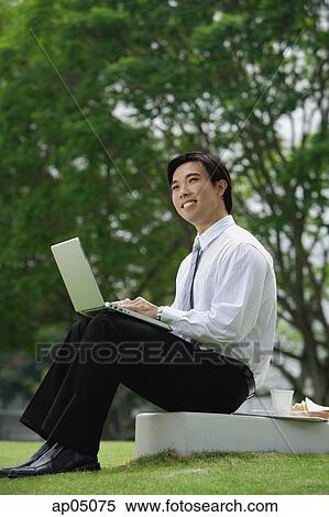 Businessman sitting in park with laptop View Large Photo Image Stock Photography - Businessman sitting in park with laptop. Fotosearch