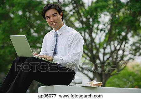 Businessman sitting in park with laptop, looking at camera View Large Photo Image Stock Photo - Businessman sitting in park with laptop, looking at camera. Fotosearch