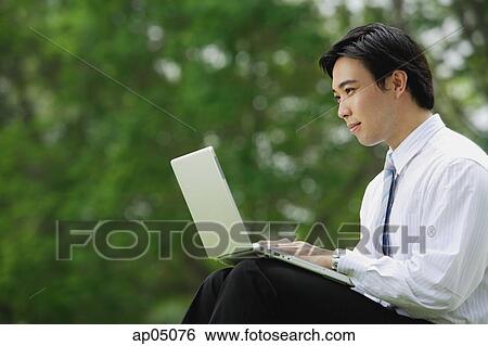 Stock Photograph - Businessman sitting in park with laptop, side view. Fotosearch