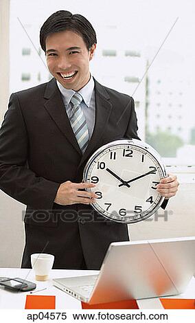 Businessman standing in front of desk, holding clock View Large Photo Image Stock Photography - Businessman standing in front of desk, holding clock. Fotosearch