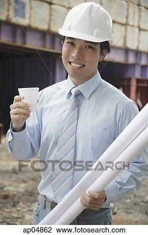 Stock Image - Businessman wearing hardhat, carrying blueprints and a cup. Fotosearch