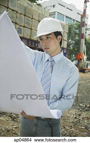 Businessman wearing hardhat, looking at blueprints View Large Photo Image Picture - Businessman wearing hardhat, looking at blueprints. Fotosearch