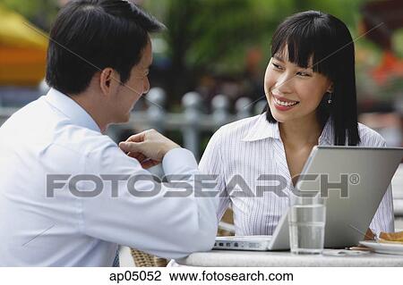 Stock Image - Businesswoman and businessman at outdoor cafe, with laptop. Fotosearch