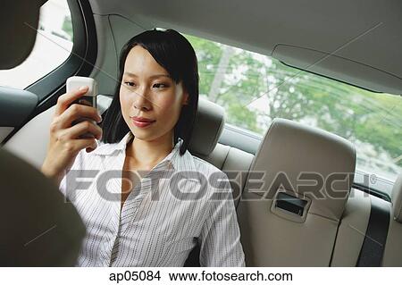 Picture - Businesswoman in backseat of car using mobile phone, text messaging. Fotosearch