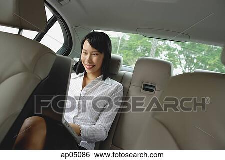 Businesswoman in backseat of car using laptop, smiling View Large Photo Image Stock Photograph - Businesswoman in backseat of car using laptop, smiling. Fotosearch