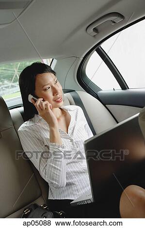 Stock Photo - Businesswoman in car using laptop and mobile phone. Fotosearch