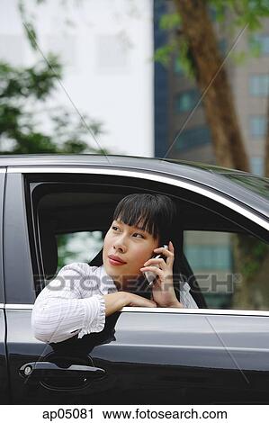 Businesswoman leaning out of car window, using mobile phone View Large Photo Image Stock Image - Businesswoman leaning out of car window, using mobile phone. Fotosearch