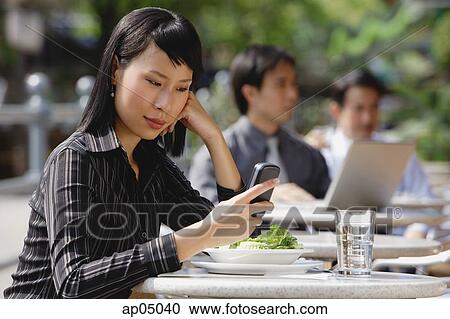 Stock Image - Businesswoman using mobile phone at outdoor cafe, text messaging. Fotosearch
