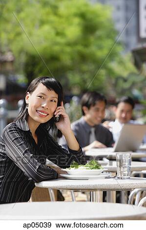 Stock Photo - Businesswoman using mobile phone at outdoor cafe, people in the background. Fotosearch