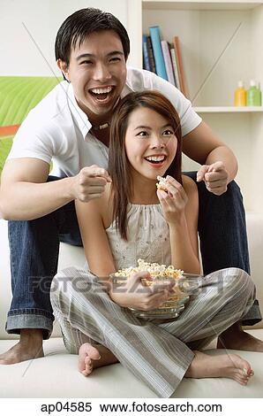 Couple at home in living room, watching TV, eating popcorn View Large Photo Image Stock Photography - Couple at home in living room, watching TV, eating popcorn. Fotosearch