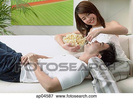 Stock Photo - Couple at home, man lying on woman's lap, woman feeding man. Fotosearch