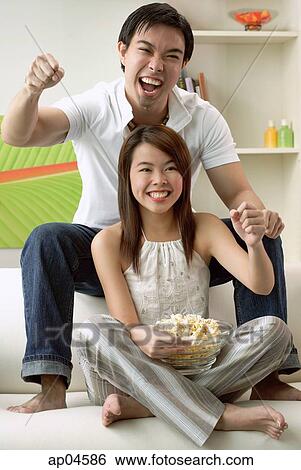 Stock Photograph - Couple in living room, man sitting on sofa, woman on floor. Fotosearch