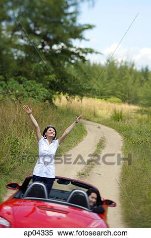Couple in red sports car, man driving, woman standing in car with arms raised View Large Photo Image Stock Photography - Couple in red sports car, man driving, woman standing in car with arms raised. Fotosearch