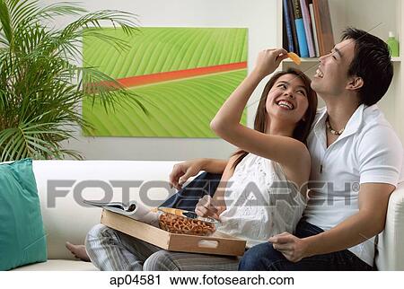 Couple sitting on sofa, woman feeding man View Large Photo Image Stock Image - Couple sitting on sofa, woman feeding man. Fotosearch