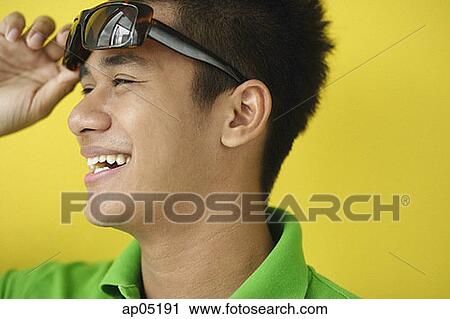 Stock Image - Man adjusting sunglasses, looking away. Fotosearch