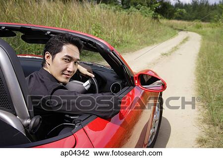 Stock Image - Man driving red convertible sports car, turning to look at camera. Fotosearch