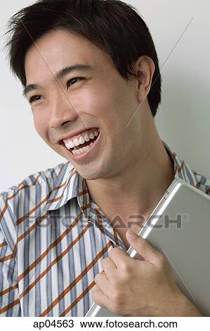 Stock Image - Man holding laptop, smiling. Fotosearch