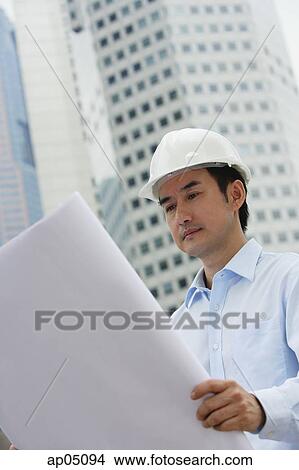 Man in hardhat, holding blueprints, building in the background View Large Photo Image Picture - Man in hardhat, holding blueprints, building in the background. Fotosearch