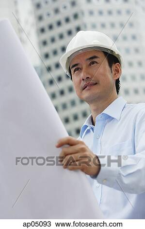 Stock Image - Man in hardhat, holding blueprints. Fotosearch