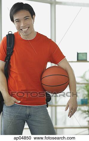 Stock Image - Man in red T shirt and jeans, holding basketball. Fotosearch