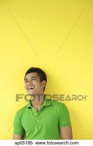 Stock Photography - Man standing against yellow wall, smiling, looking up. Fotosearch