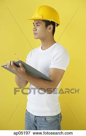 Man wearing hardhat, holding clipboard, looking away View Large Photo Image Stock Photo - Man wearing hardhat, holding clipboard, looking away. Fotosearch