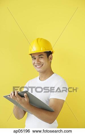 Stock Photograph - Man wearing hardhat, holding clipboard. Fotosearch